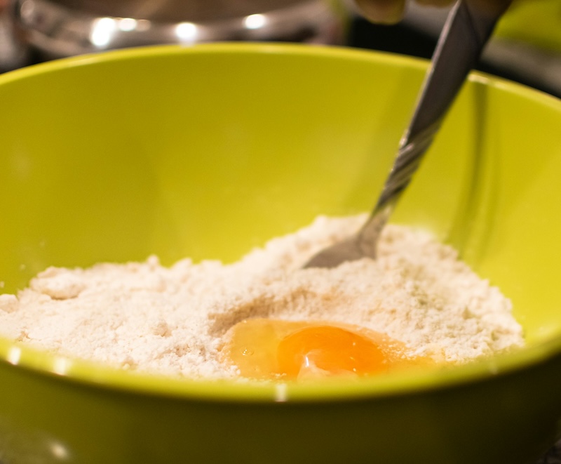 A spoon stirring ingredients including egg and flour in a yellow bowl